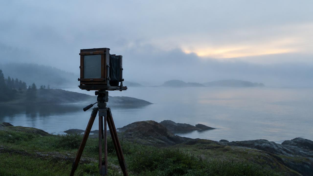 Large-format wooden field camera on a tripod facing a misty coastline at dawn